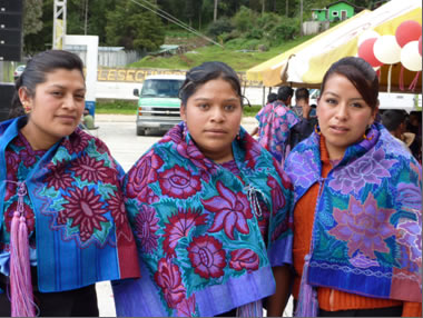 3 women wearing red ad purpols flowers embrodered on a blue shawl