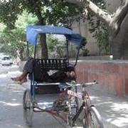view of rickshaw puller from behind showing puller reclining in front with legs sticking out