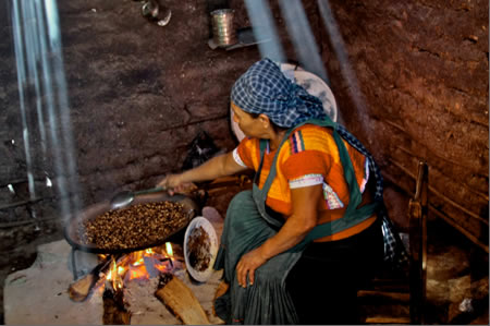 woman artisan sitting and toasting coffee in large circular pan over a fire
